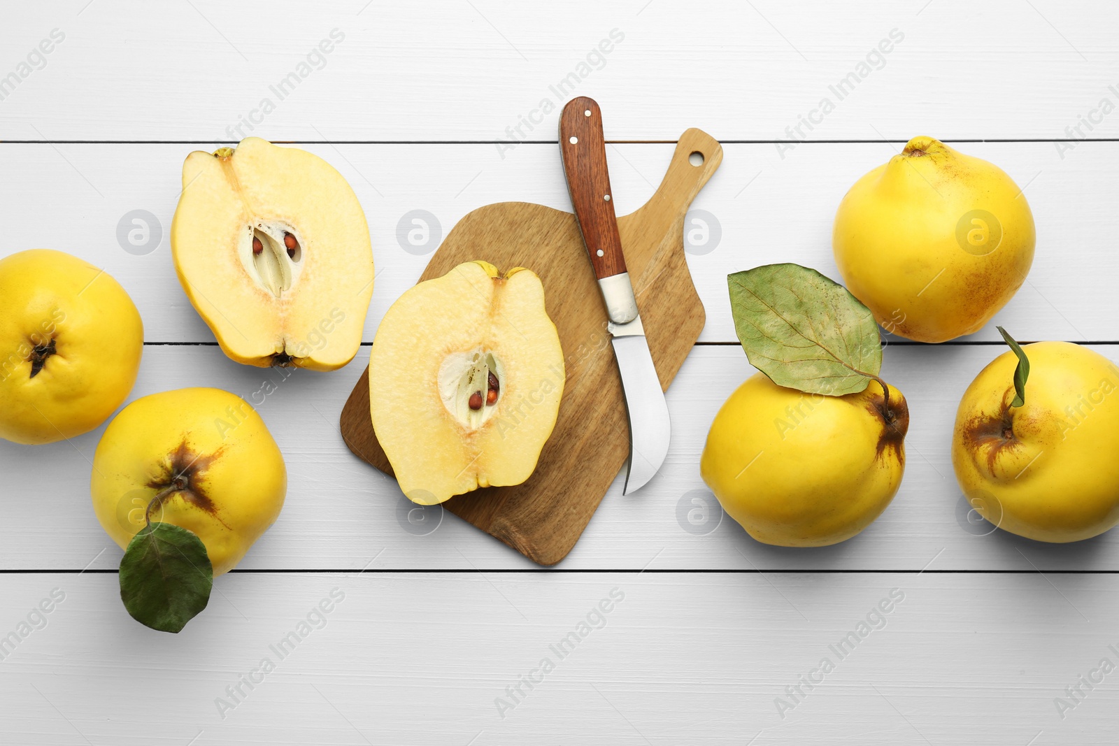 Photo of Tasty ripe quince fruits and knife on white wooden table, flat lay