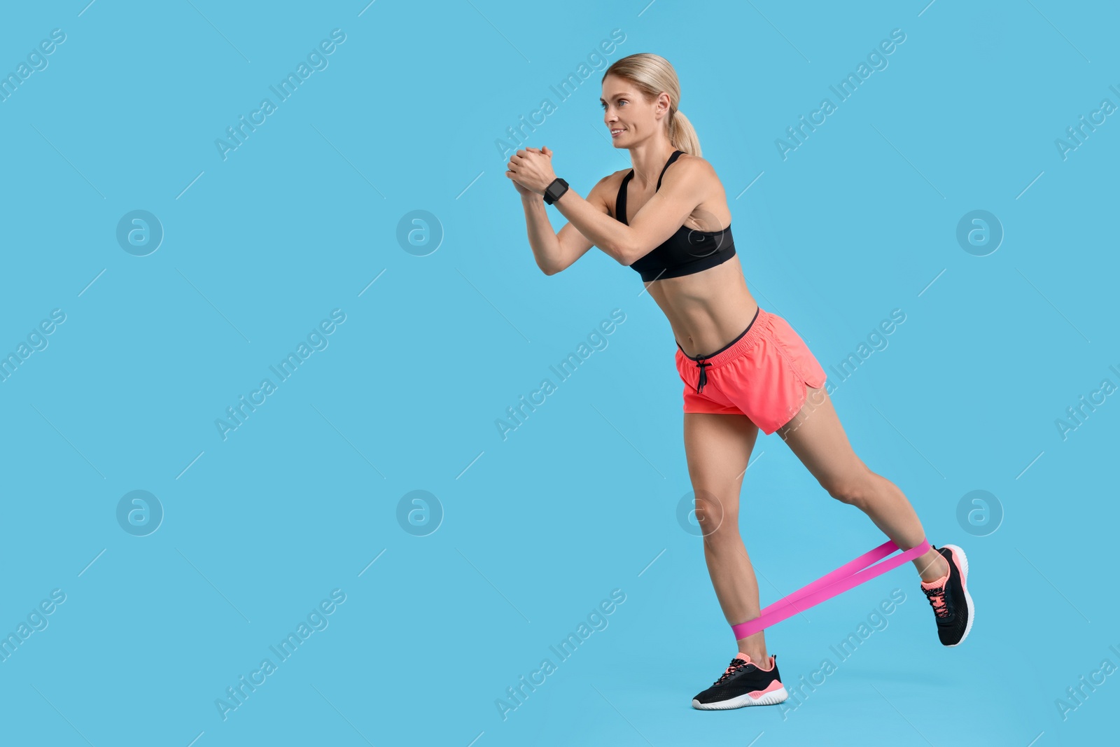 Photo of Woman exercising with elastic resistance band on light blue background. Space for text