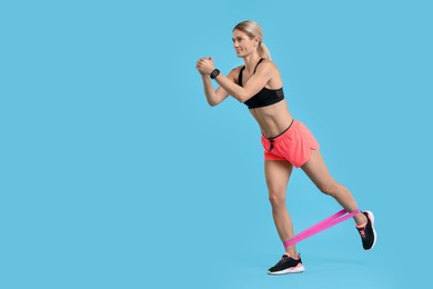 Woman exercising with elastic resistance band on light blue background. Space for text