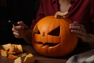 Photo of Woman carving pumpkin for Halloween at wooden table, closeup