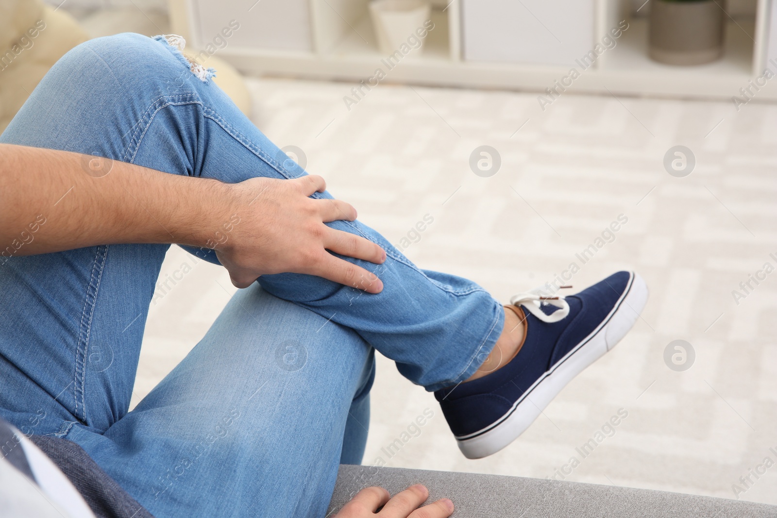 Photo of Man suffering from leg pain at home, closeup