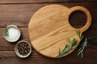 Photo of Cutting board, salt, pepper and rosemary on wooden table, flat lay. Space for text