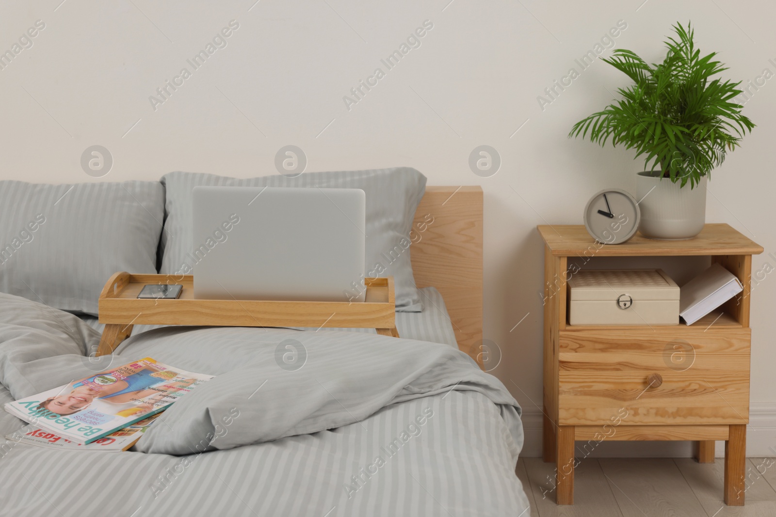 Photo of Wooden tray table with laptop and smartphone on bed indoors