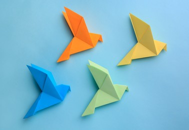 Origami art. Colorful handmade paper birds on light blue background, flat lay