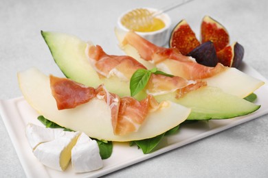 Photo of Tasty melon, jamon and figs served on light grey table, closeup