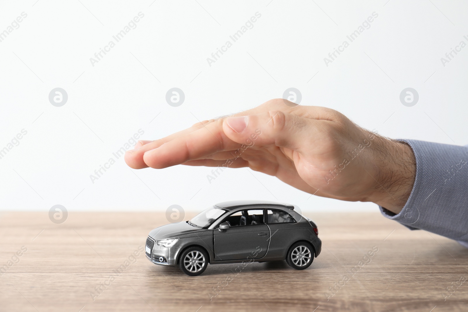 Photo of Male insurance agent covering toy car at table, closeup