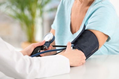 Nurse measuring blood pressure of elderly woman indoors, closeup. Assisting senior generation