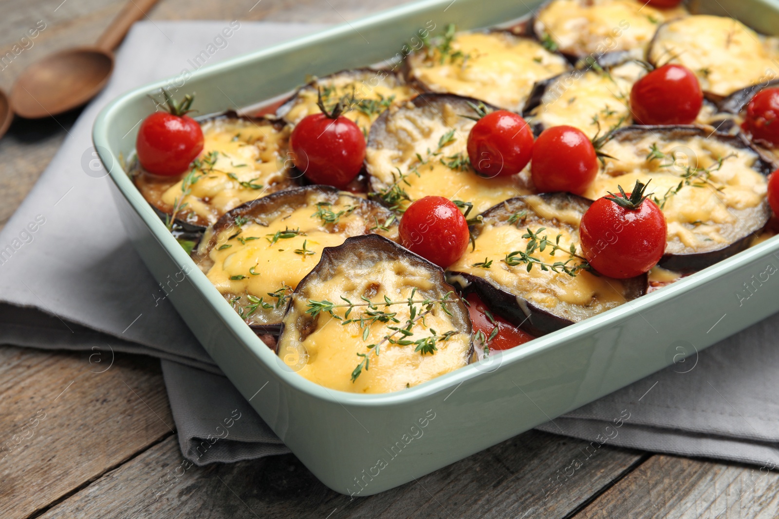 Photo of Baked eggplant with tomatoes and cheese in dishware on wooden table, closeup