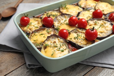 Baked eggplant with tomatoes and cheese in dishware on wooden table, closeup