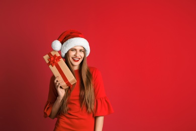 Young beautiful woman in Santa hat with gift box on color background. Christmas celebration