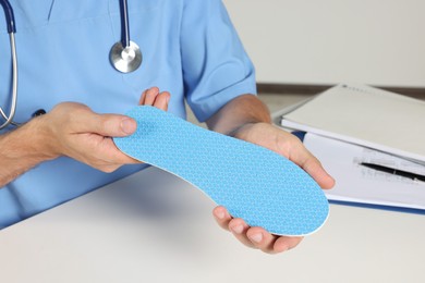 Male orthopedist showing insole in hospital, closeup