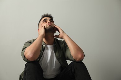 Photo of Sad man sitting near light grey wall. Space for text