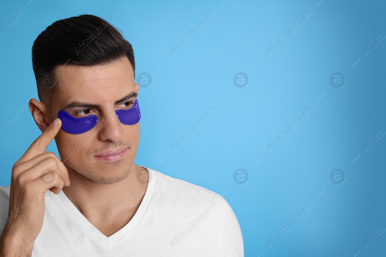 Photo of Man applying under eye patch on light blue background. Space for text