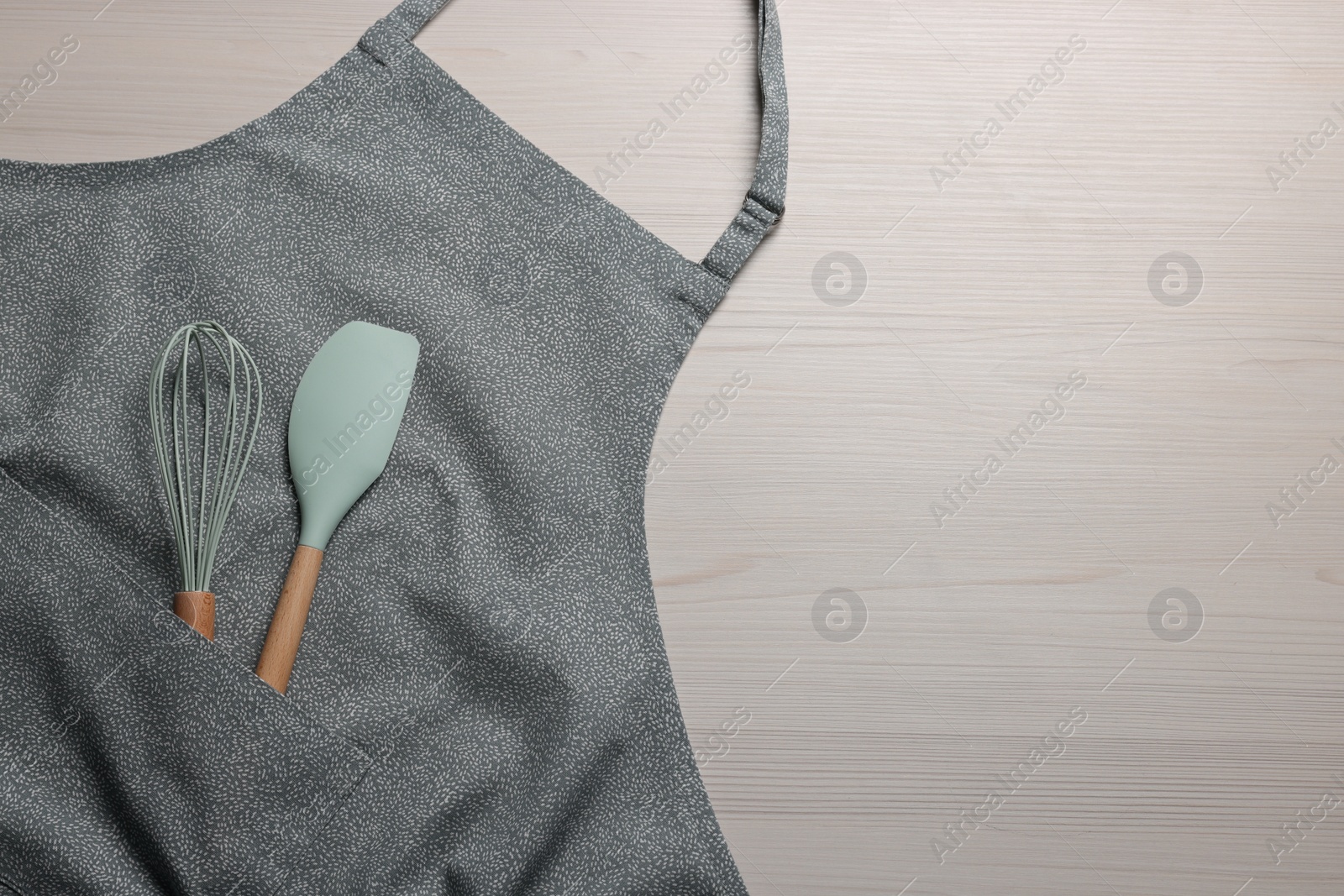 Photo of Stylish apron, spatula and whisk on white wooden table, top view. Space for text