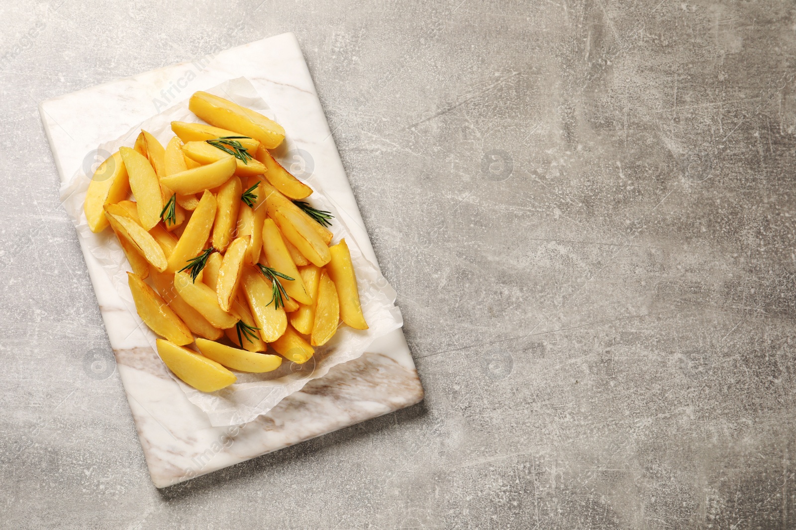 Photo of Tasty baked potato wedges and rosemary on grey table, top view. Space for text