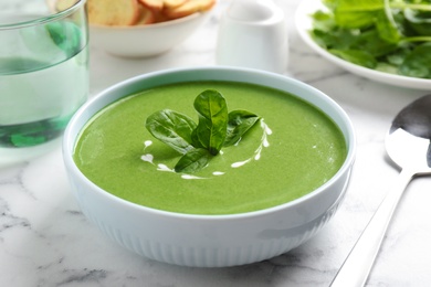 Bowl of healthy green soup with fresh spinach on marble table