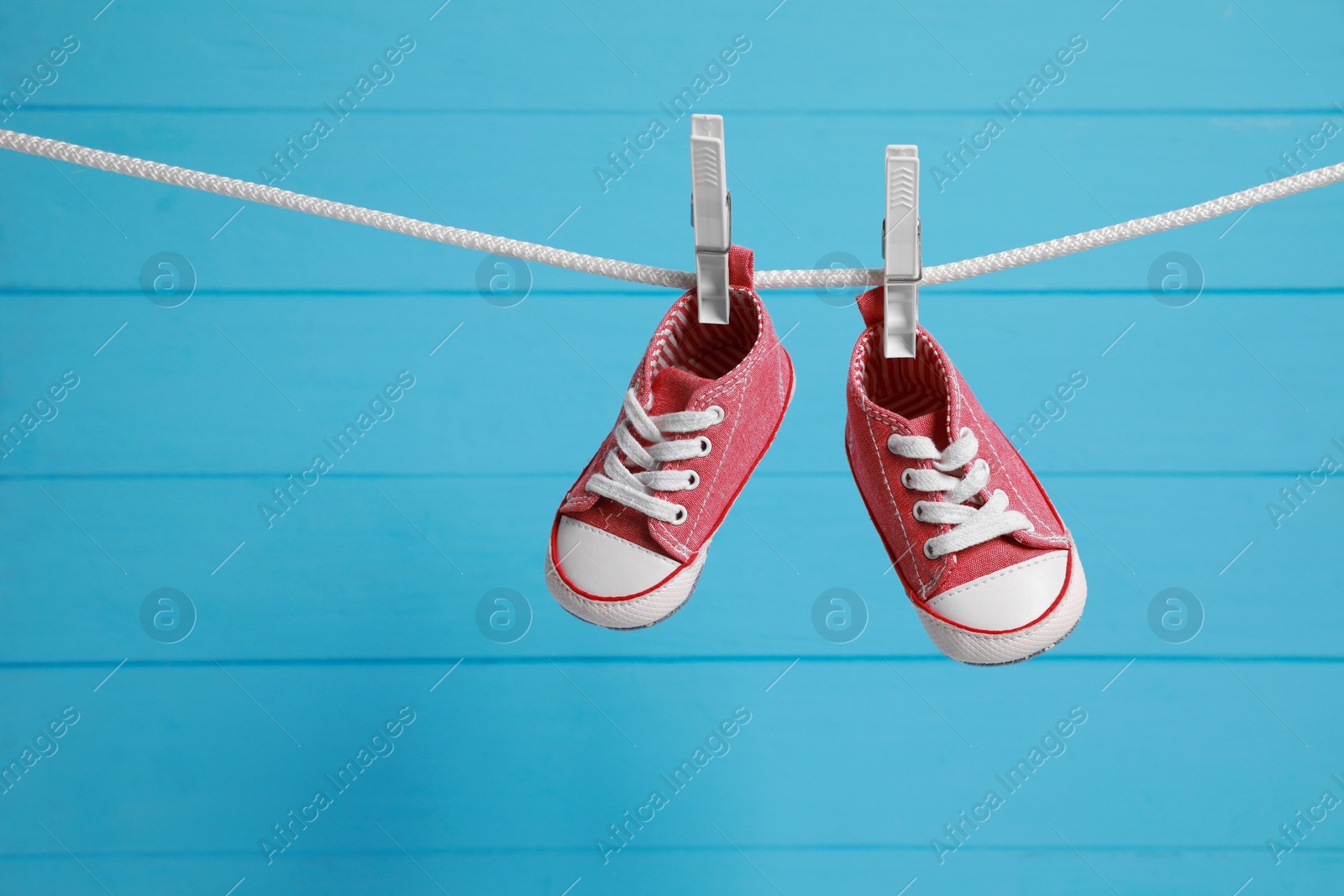 Photo of Cute baby sneakers drying on washing line against light blue wooden wall. Space for text