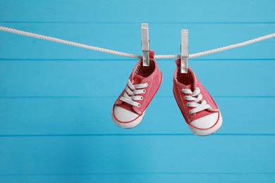 Cute baby sneakers drying on washing line against light blue wooden wall. Space for text