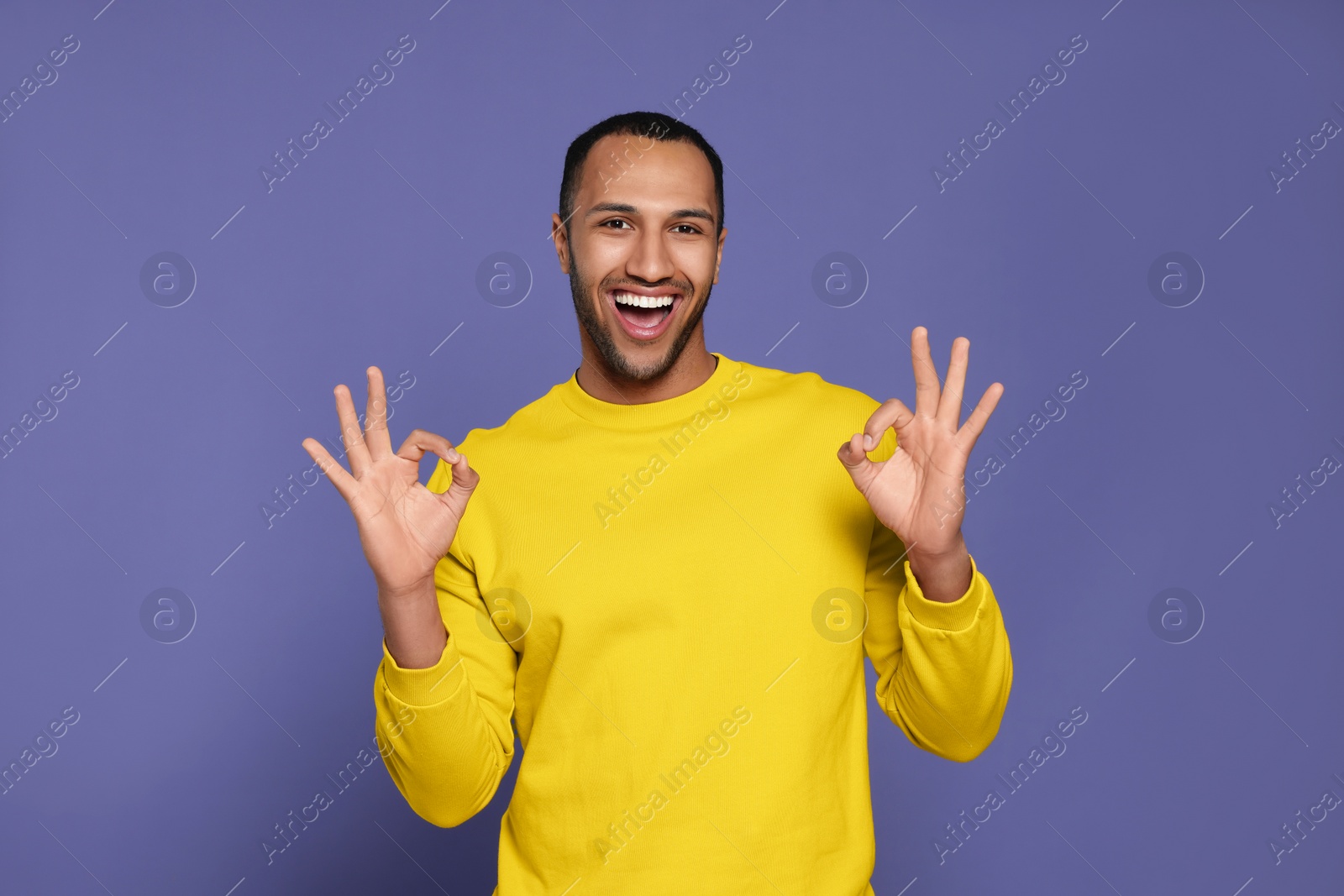 Photo of Happy African American man showing ok gesture on purple background