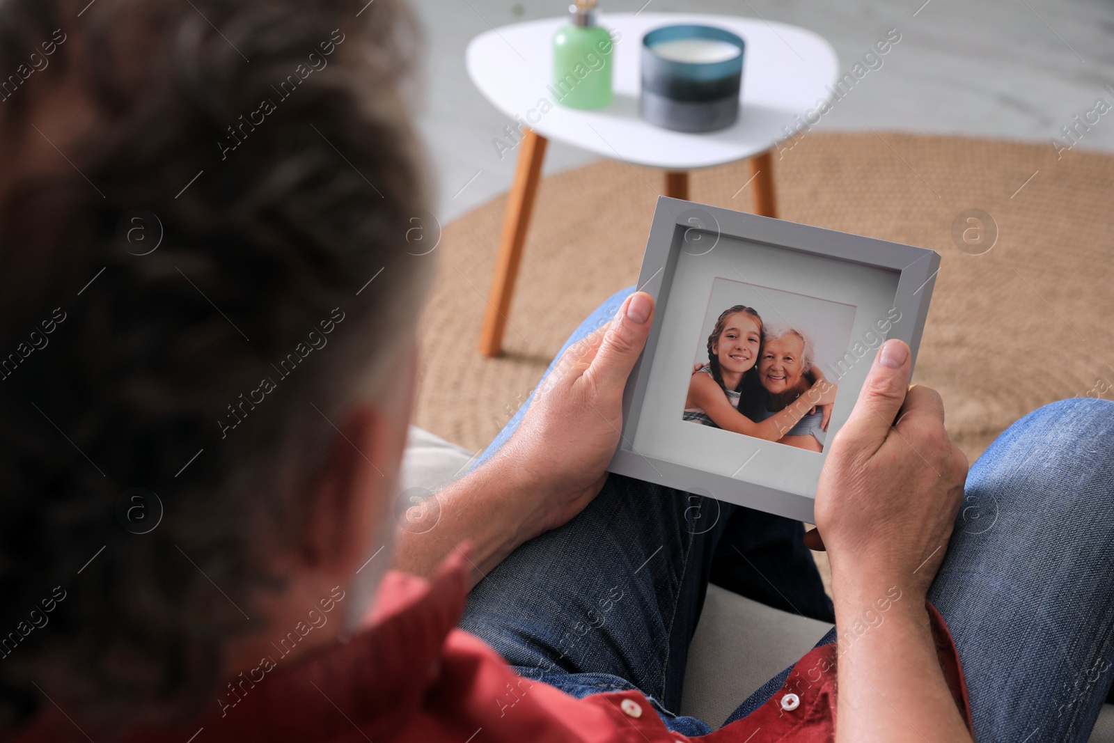 Photo of Senior man holding frame with photo of his wife and granddaughter at home, closeup