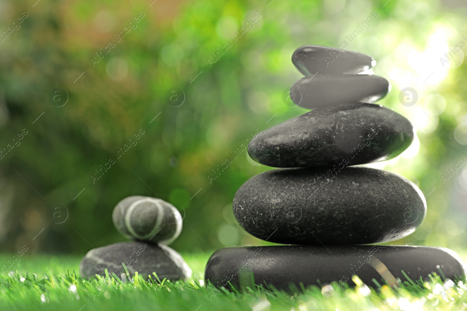 Photo of Stacks of stones on green grass against blurred background, space for text. Zen concept