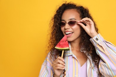 Beautiful young African American woman with piece of watermelon on yellow background. Space for text