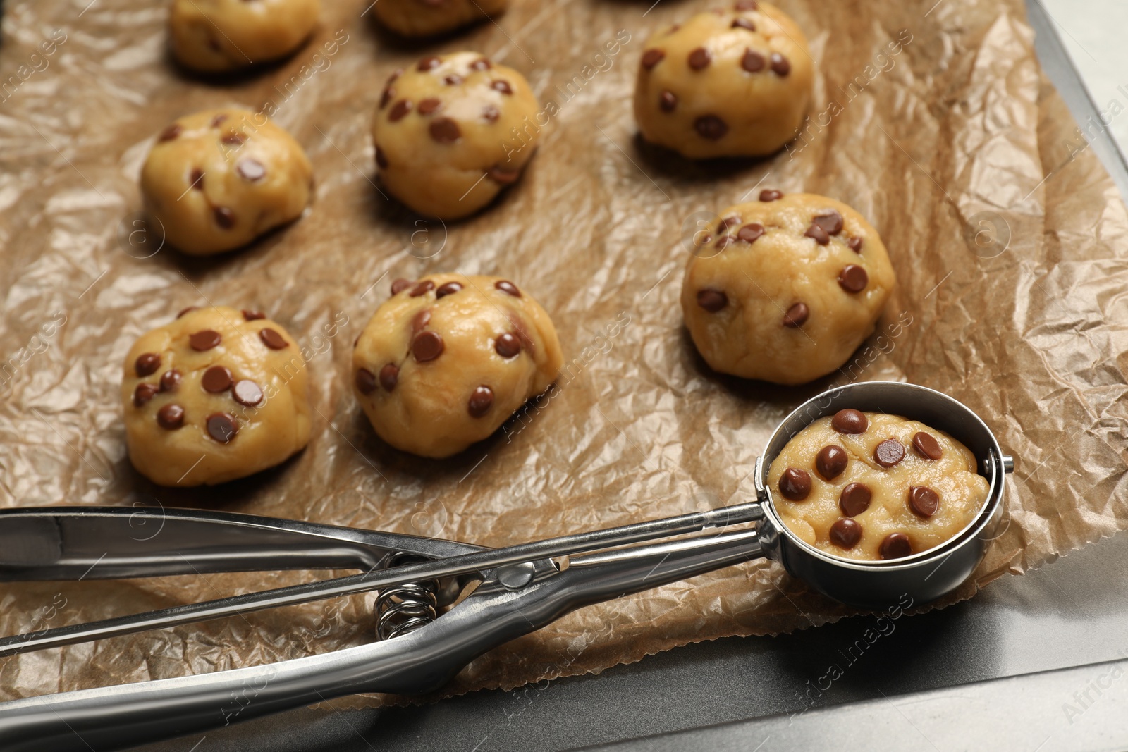 Photo of Uncooked chocolate chip cookies and scoop on parchment, closeup