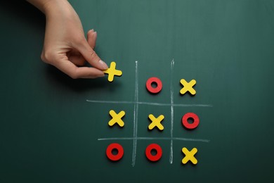 Photo of Woman playing tic tac toe game on green chalkboard, top view