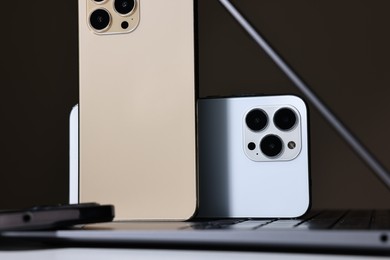 Modern laptop and smartphones on white table against brown background, closeup