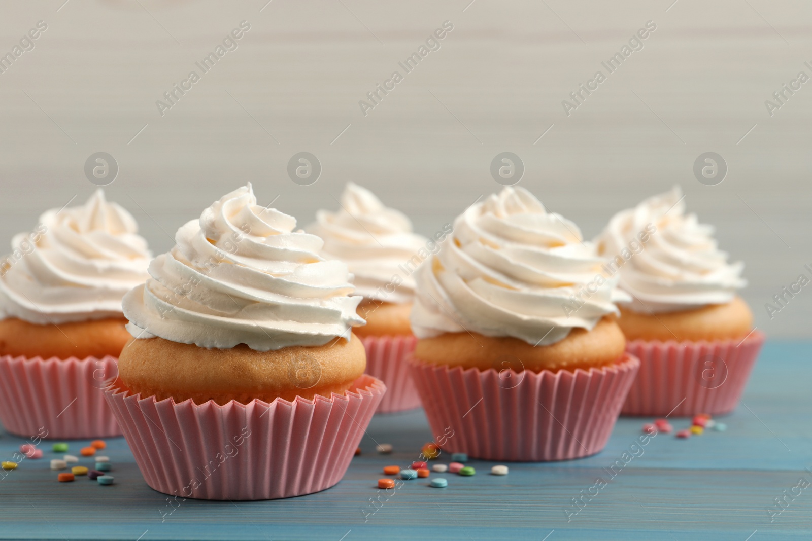 Photo of Delicious cupcakes decorated with cream on light blue wooden table