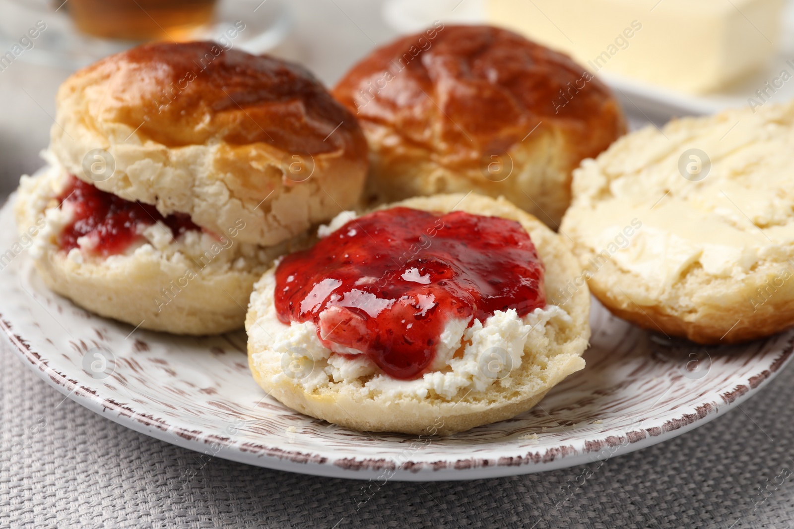 Photo of Freshly baked soda water scones with cranberry jam and butter on light grey mat, closeup