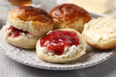 Freshly baked soda water scones with cranberry jam and butter on light grey mat, closeup