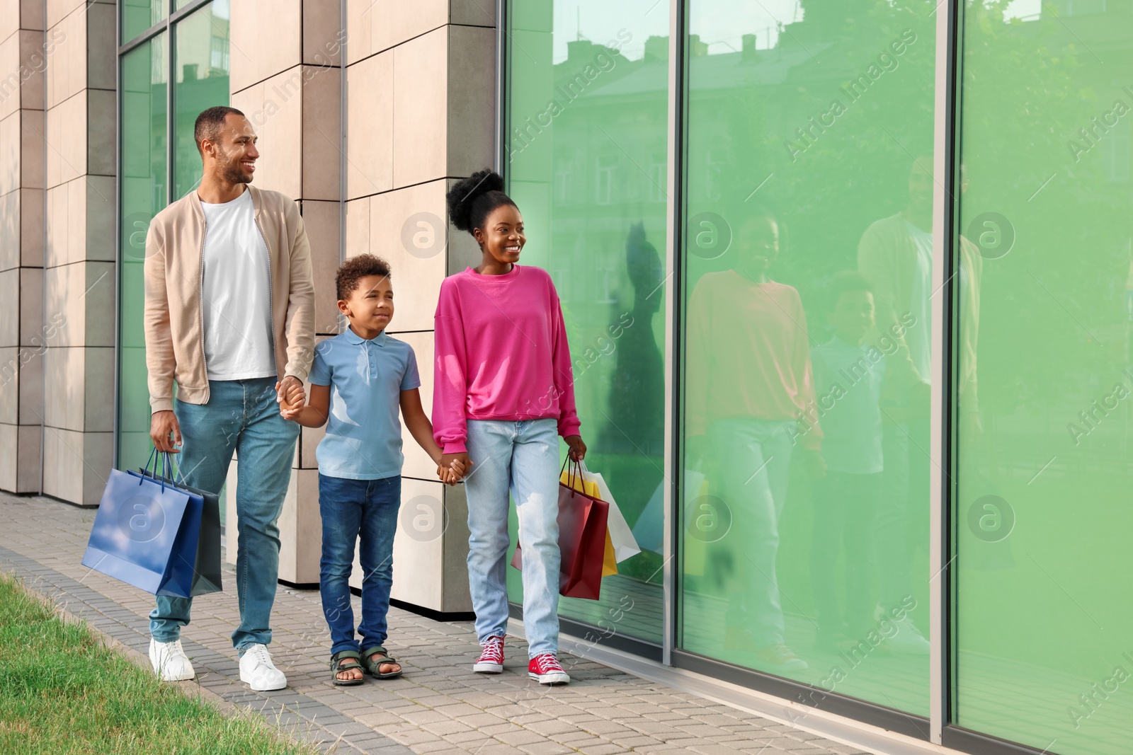 Photo of Family shopping. Happy parents and son with colorful bags near mall outdoors