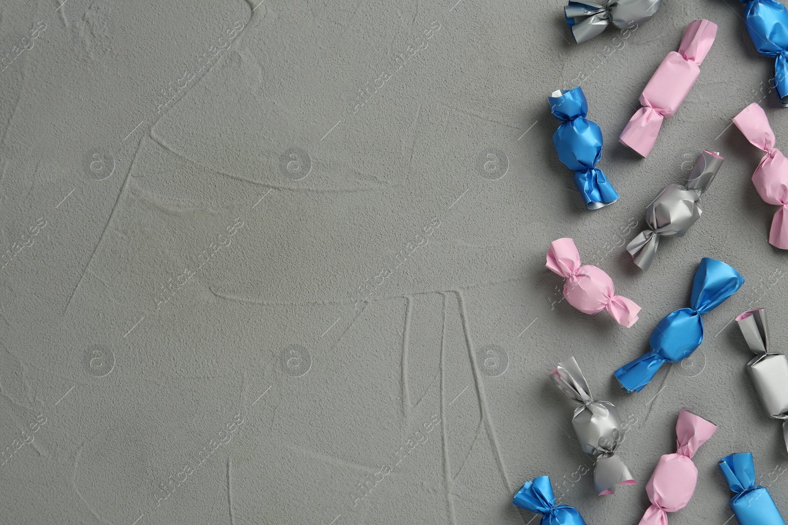 Photo of Candies in colorful wrappers on grey table, flat lay. Space for text