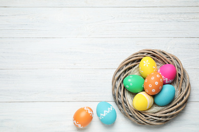 Photo of Decorative nest with Easter eggs on white wooden background, top view. Space for text