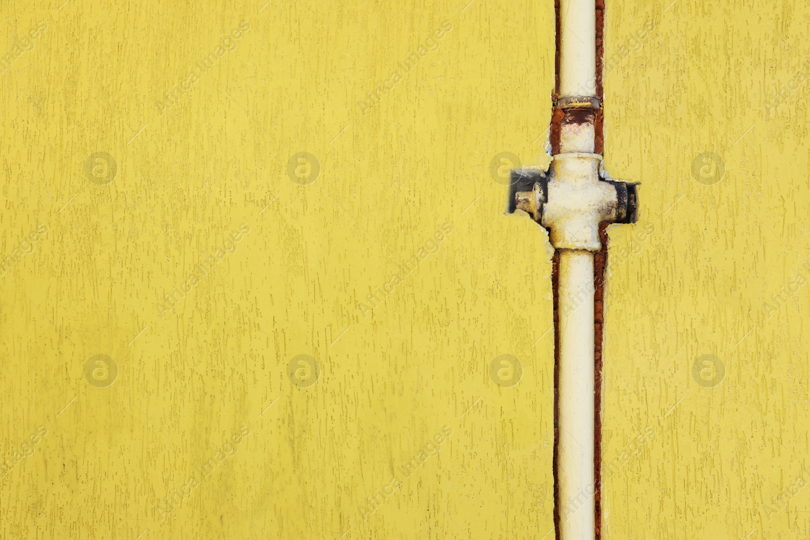 Photo of Rusty gas pipe installed in yellow wall outdoors, space for text