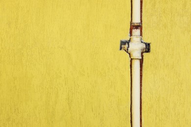 Photo of Rusty gas pipe installed in yellow wall outdoors, space for text