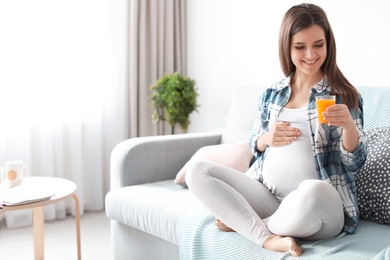 Photo of Young pregnant woman holding glass with juice at home