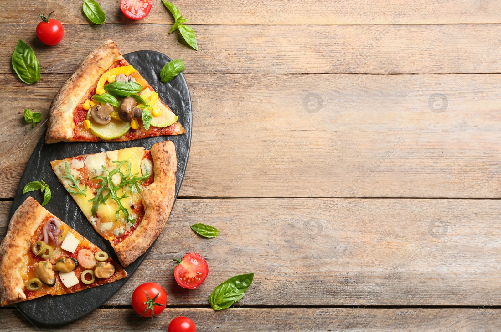 Photo of Slices of different pizzas on wooden table, flat lay. Space for text