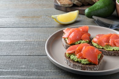 Delicious sandwiches with salmon and avocado on grey wooden table. Space for text