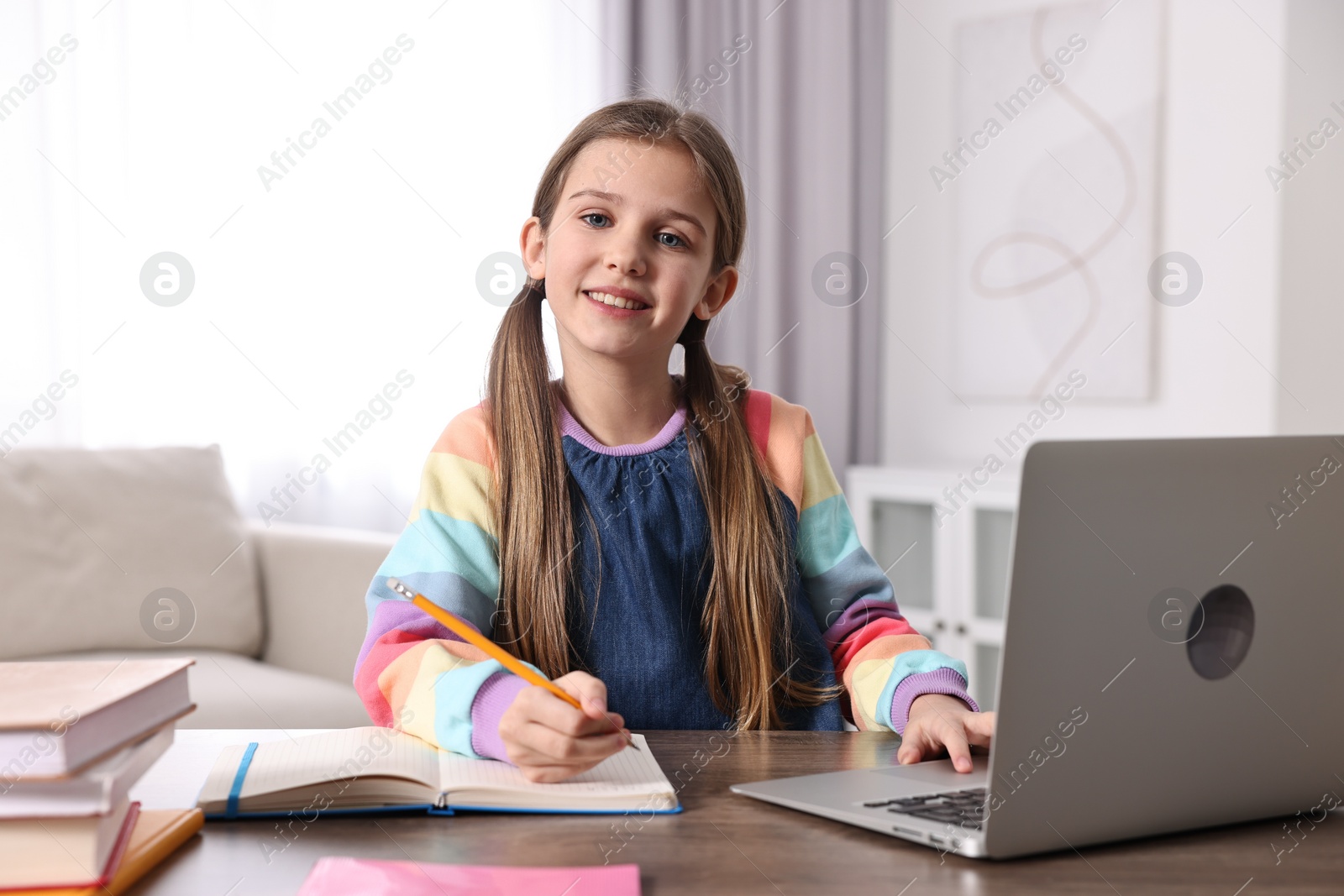 Photo of E-learning. Cute girl taking notes during online lesson at table indoors