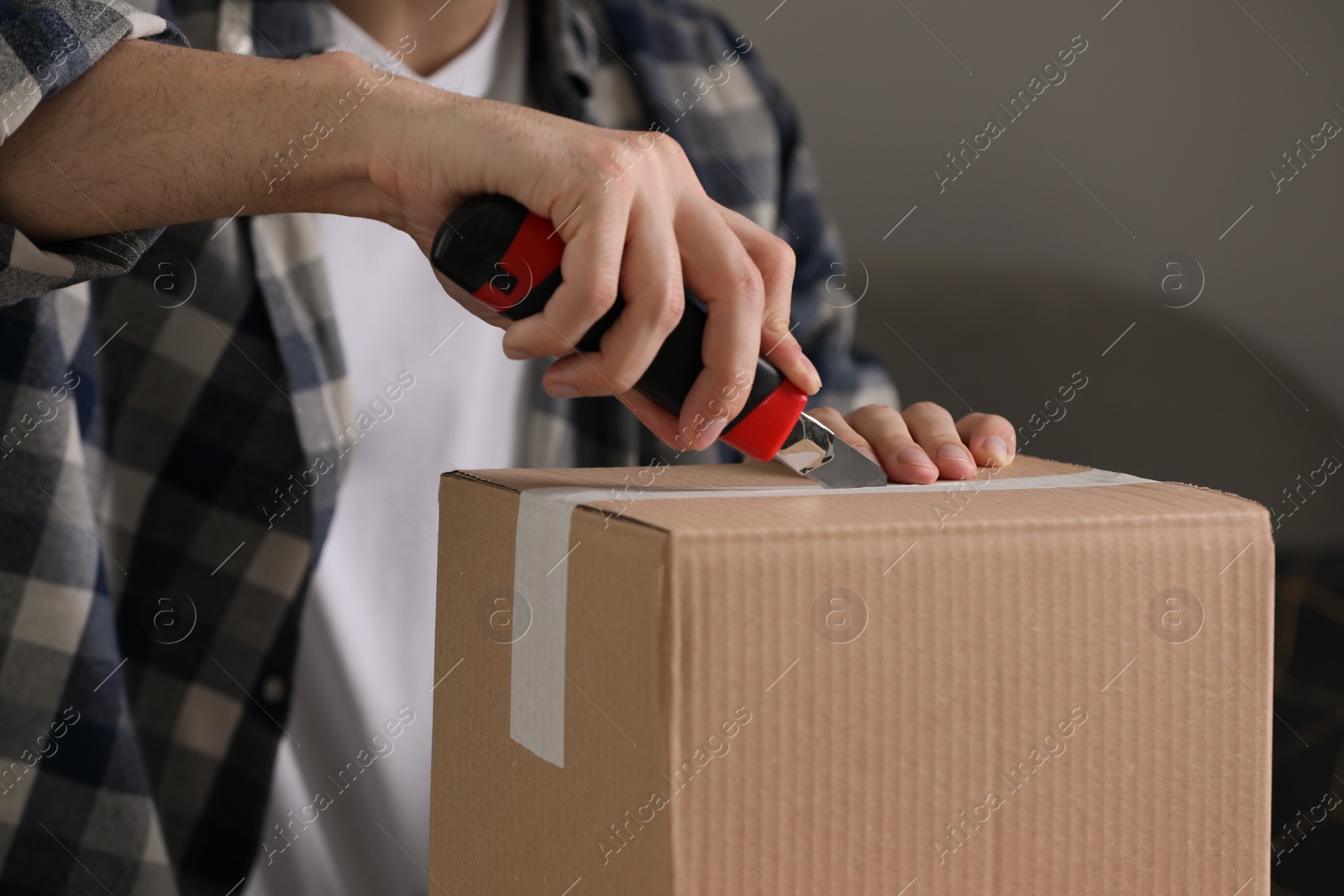 Photo of Man using utility knife to open parcel indoors, closeup