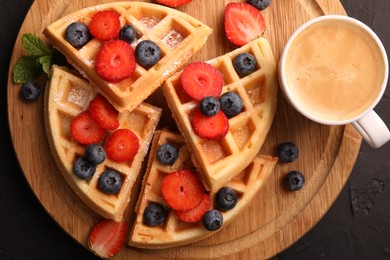 Photo of Tasty Belgian waffles with fresh berries and cup of coffee on black table, top view
