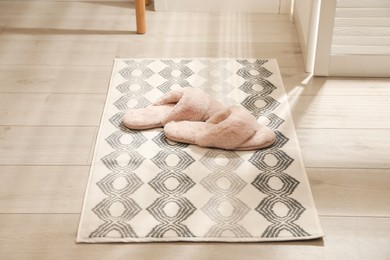 Photo of New stylish bath mat with fluffy slippers on floor indoors