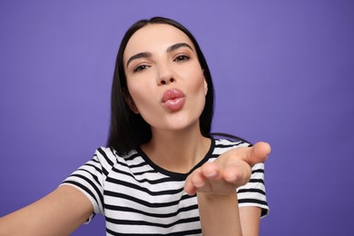 Photo of Beautiful young woman taking selfie while blowing kiss on purple background