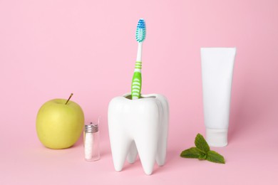 Photo of Tooth shaped holder with toothbrush, paste and apple on pink background