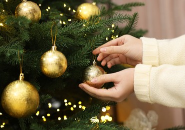 Photo of Woman decorating fir tree with golden Christmas ball indoors, closeup