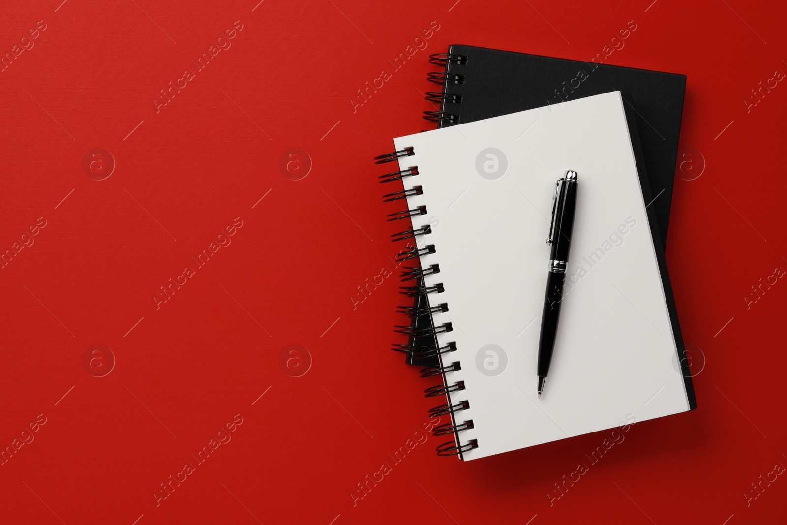 Photo of Notebooks and pen on red background, top view. Space for text