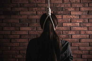 Woman with rope noose on neck near brick wall, back view