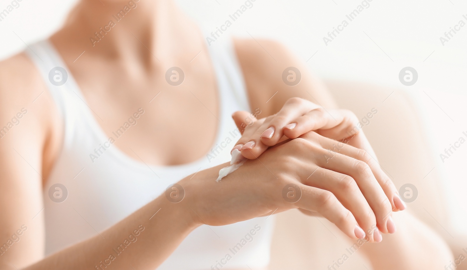 Photo of Young woman applying body cream at home